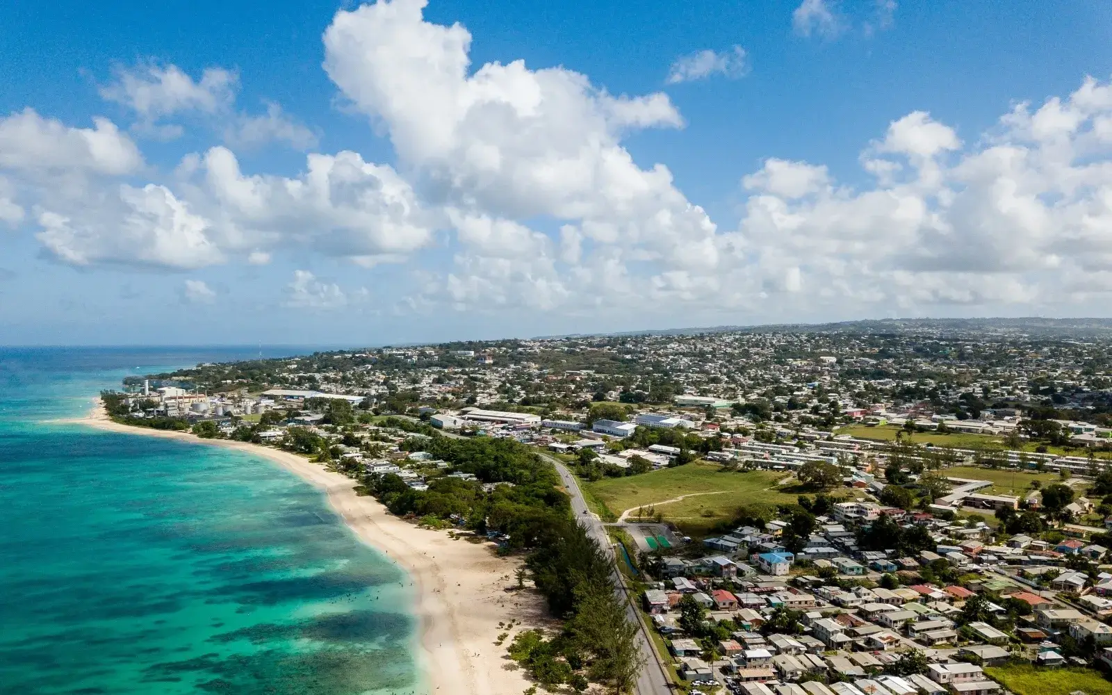 Aerial view of Barbados’ coastline with a sandy beach, turquoise sea, coastal road and residential neighbourhoods